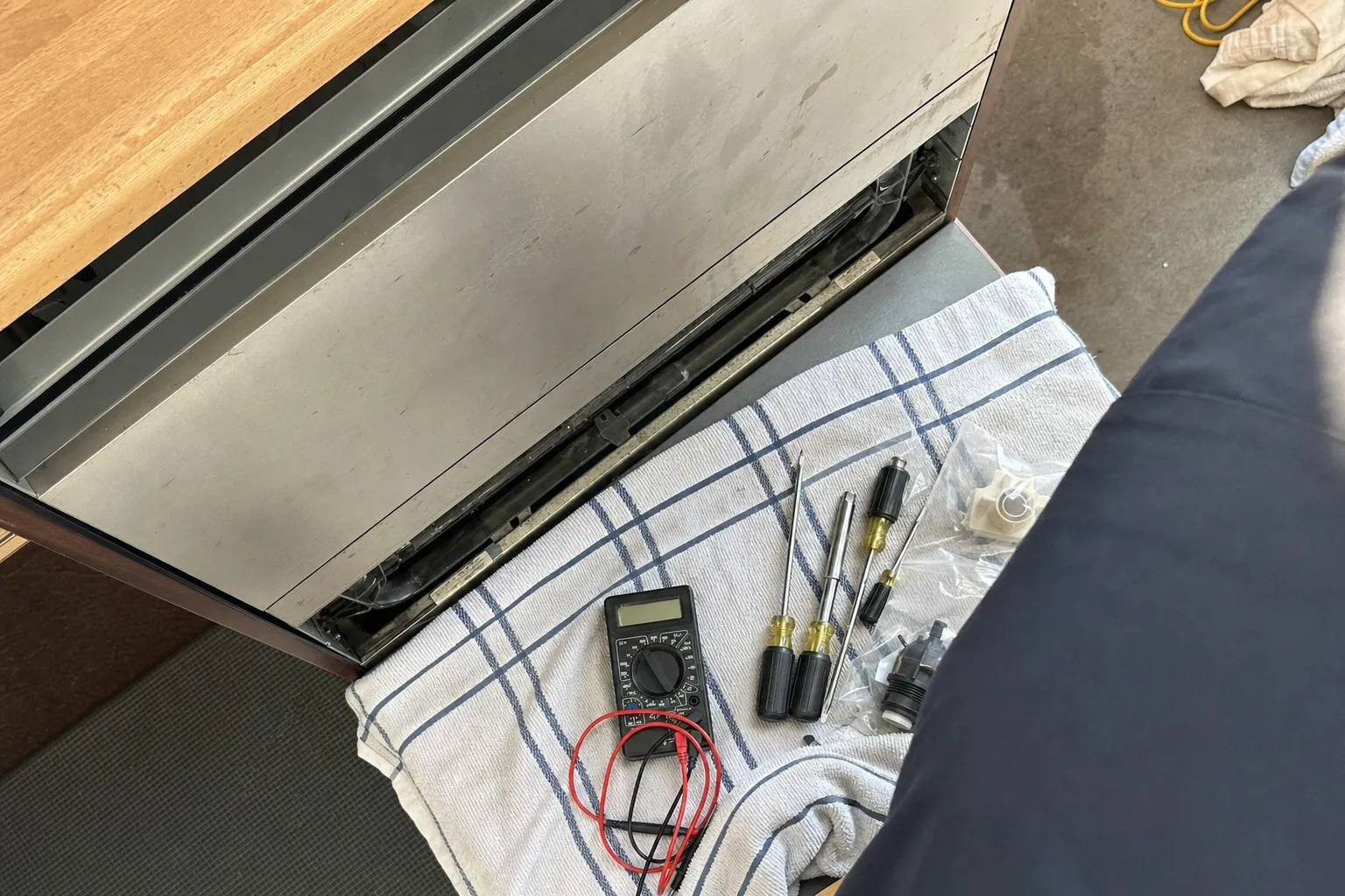 Undercounter stainless unit with its lower panel open, a multimeter and nut drivers laid out on a folded towel